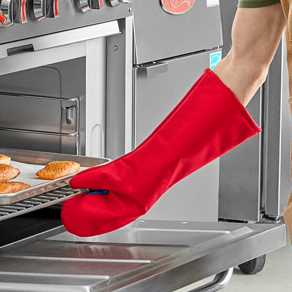 A person wearing a Tucker Safety red oven mitt holding food in a pan.