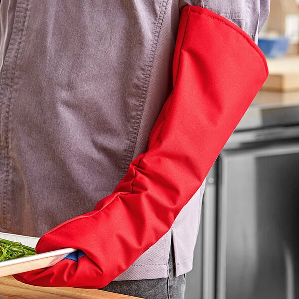 A person wearing a red Tucker Safety oven mitt holding a tray of food.