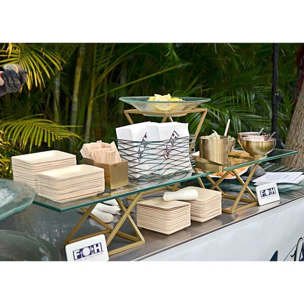 A table with a Front of the House Twist Matte Brass Riser Set holding plates and bowls.