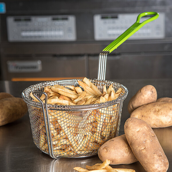 A Carlisle medium mesh fryer basket filled with french fries and a green spatula.
