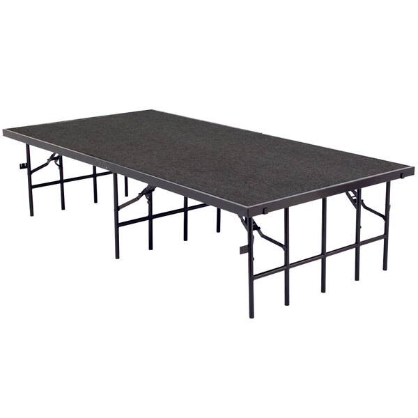 A National Public Seating portable stage with gray carpet on a black rectangular table.