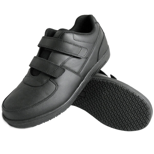 A pair of black shoes with hook and loop (Velcro) closures and textured non-slip soles.