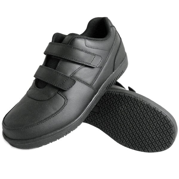 A pair of black shoes with hook and loop (Velcro) closures and textured non-slip soles.