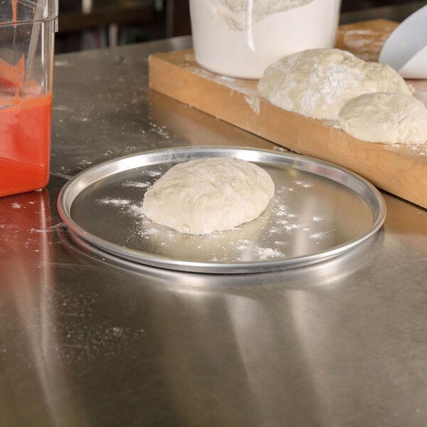 An American Metalcraft aluminum pizza pan with dough on it on a counter.