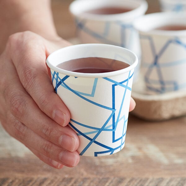 A hand holding a Choice white paper cold cup with blue and white lines filled with liquid.