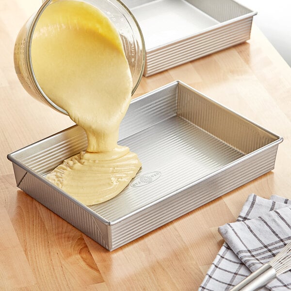 A person pouring batter into a Chicago Metallic rectangular cake pan.