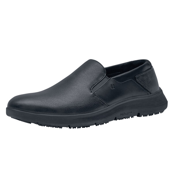A black Shoes For Crews men's slip on shoe with a white background.