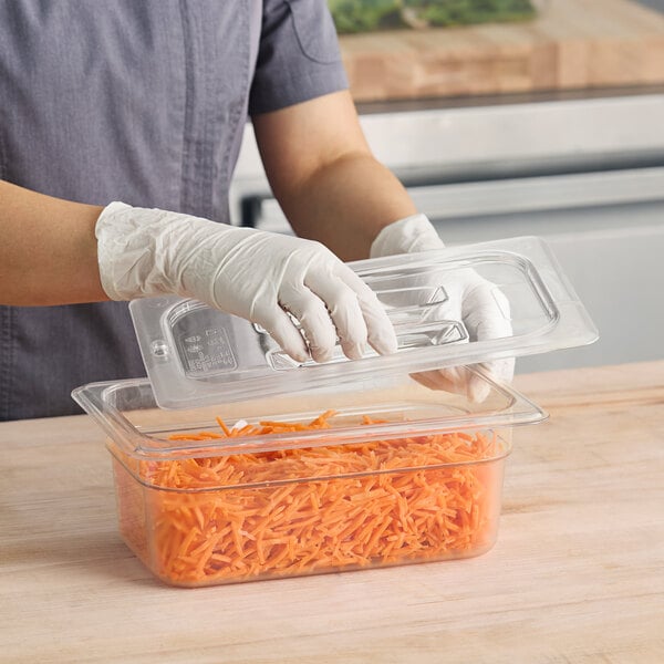 A hand in a glove places a Cambro clear plastic lid on a food container.