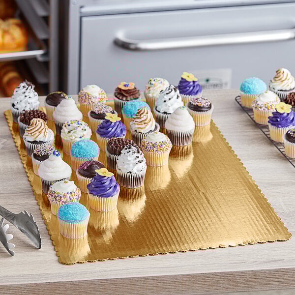 A gold laminated rectangular corrugated cake pad on a table with cupcakes on it.