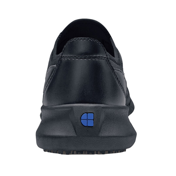 A black Shoes For Crews Karina women's athletic shoe with a blue square logo on the back.