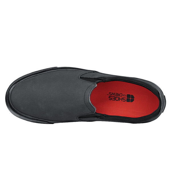A black Shoes For Crews slip-on shoe with red soles.