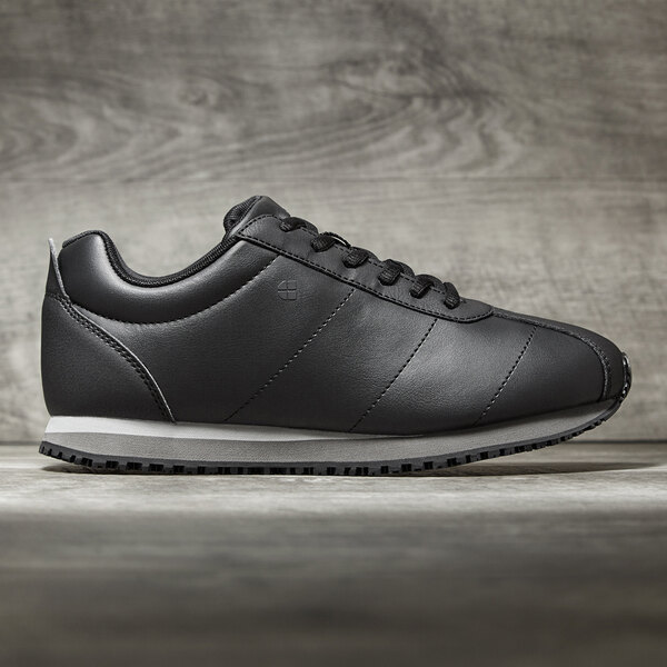 A black Shoes For Crews women's sneaker with white sole.