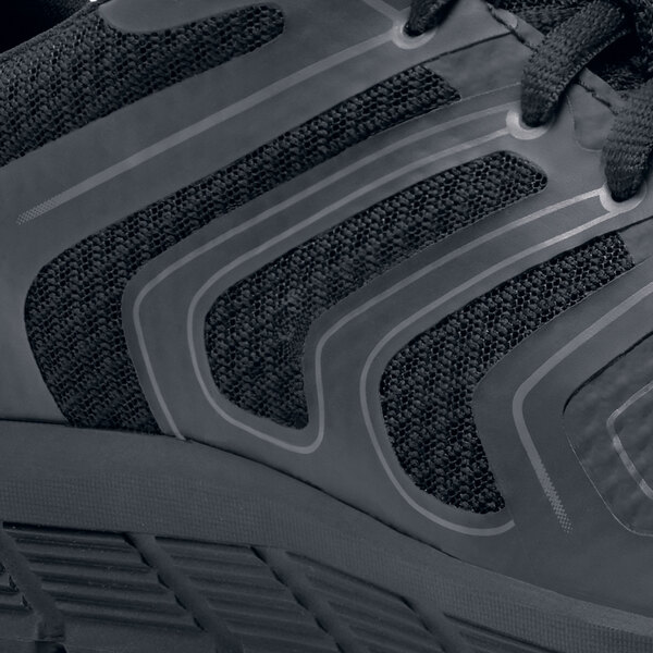 A close up of a black and grey Shoes For Crews Stride athletic shoe with a reflective stripe.