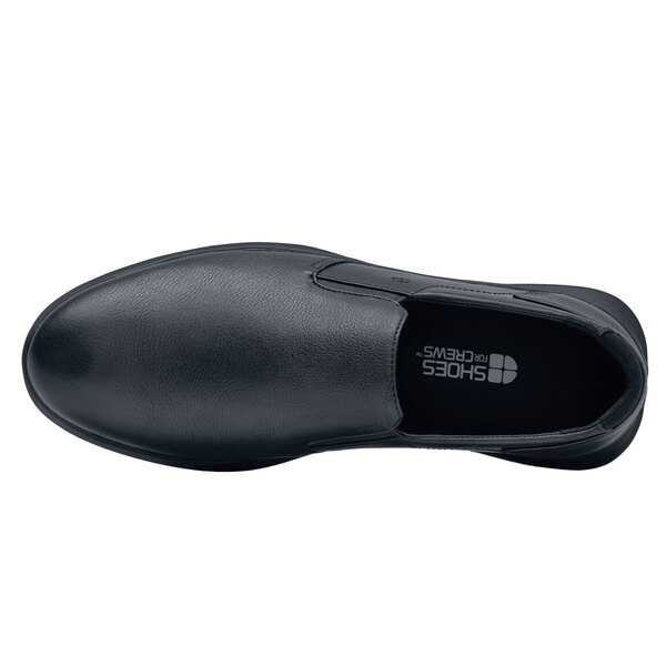 A black Shoes For Crews slip-on shoe with a rubber sole and white logo.
