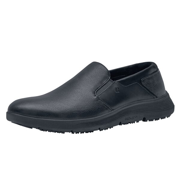 A black Shoes For Crews men's slip-on shoe with a white background.