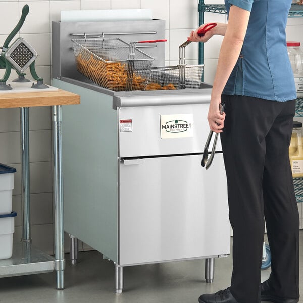 A commercial stainless steel floor fryer with baskets, used for deep frying food in a kitchen setting.