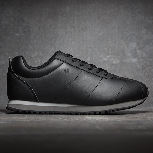 A black Shoes For Crews sneaker with a grey surface.