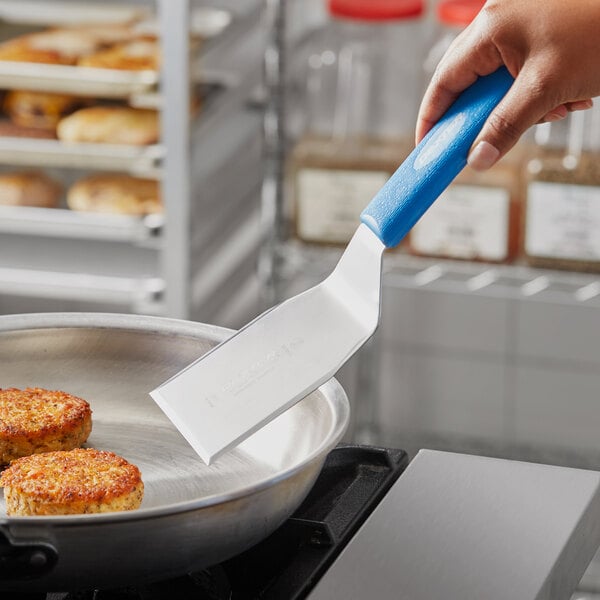 A hand holding a blue Dexter-Russell Sani-Safe hamburger turner cutting food.