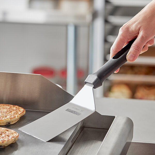 A hand holding a Victorinox flex turner with a black handle cooking food on a pan.