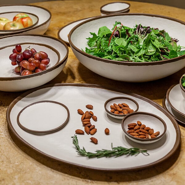 A table with bowls of green salad, grapes, and nuts, including a GET glazed cream melamine bowl with brown trim.