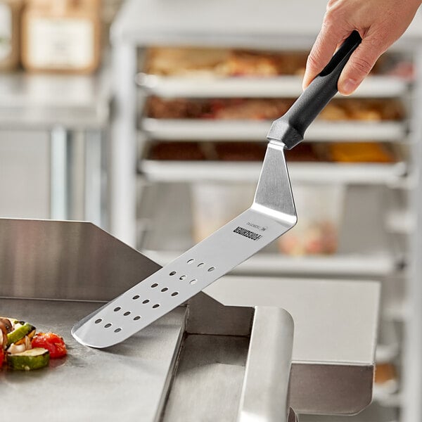 A hand holding a Victorinox perforated turner over a grill.