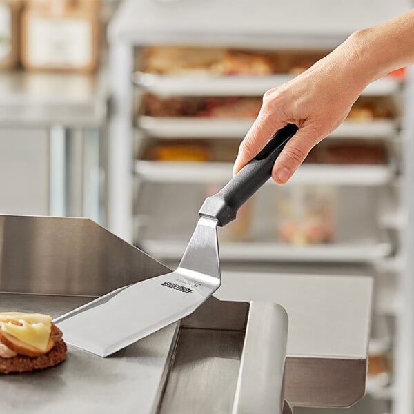 A hand holding a Victorinox hamburger turner with a black handle over food.