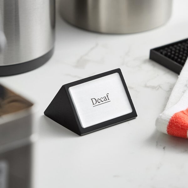 A small black wood sign with a silver face displaying the word 'Decaf'.