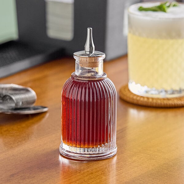 A Barfly ribbed glass bitters bottle on a table with liquid inside.