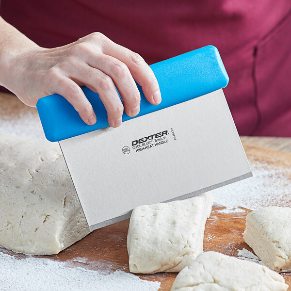 A person using a Dexter Russell Cool Blue dough cutter to cut dough on a cutting board.