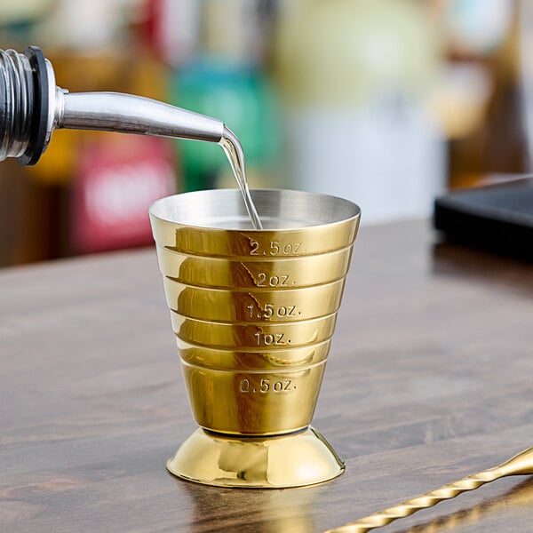 A gold-plated Barfly measuring jigger with a shot glass on top.