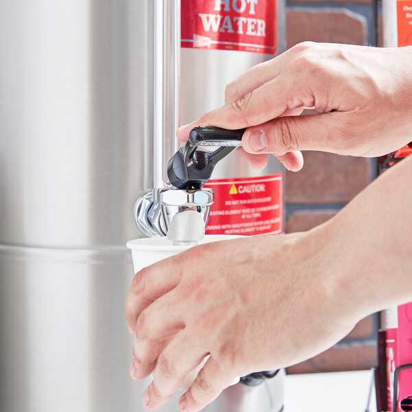 A person using a Grindmaster hot water dispenser to fill a water bottle.