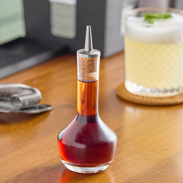 A Barfly glass bitters bottle of liquid with a cork on a table.
