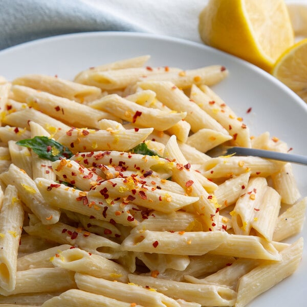 A plate of pasta with a fork and lemons with Regal Mild Crushed Red Pepper on the table.