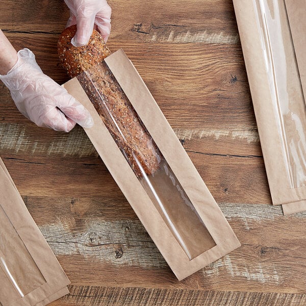 A person in gloves holding a Durable Packaging kraft paper windowed bread bag with a loaf of bread inside.