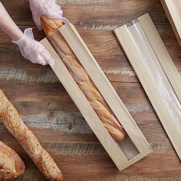 A person holding a baguette in a Durable Packaging paper bag with a window.
