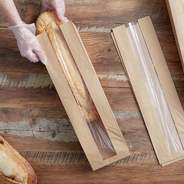 A hand holding a Durable Packaging Kraft paper bag with a loaf of bread inside.