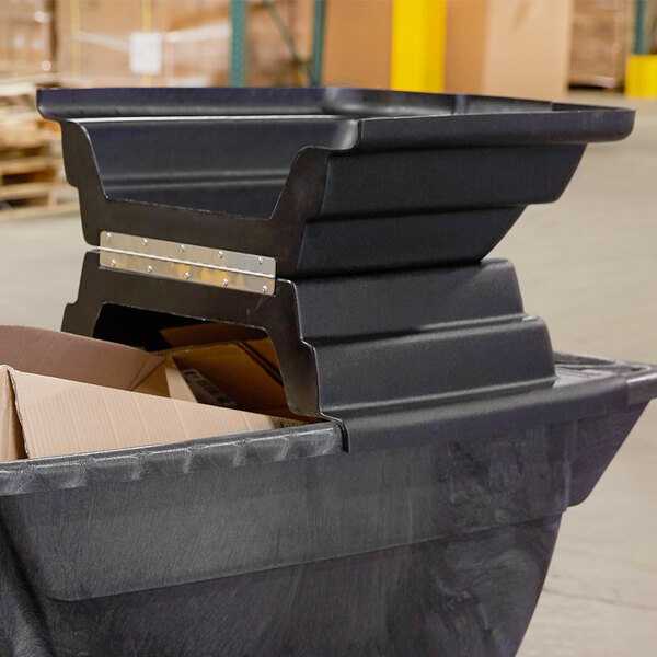 A close-up of a black Rubbermaid tilt truck with a hinged dome lid.