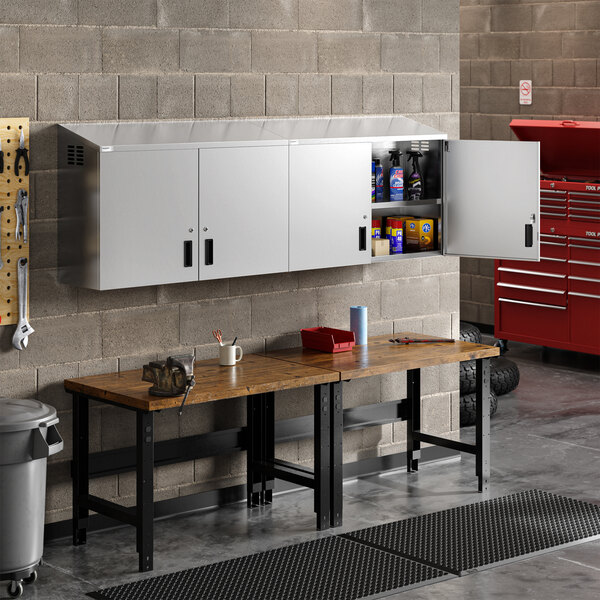 A large stainless steel wall cabinet with hinged doors mounted above a workbench in a garage or workshop setting.
