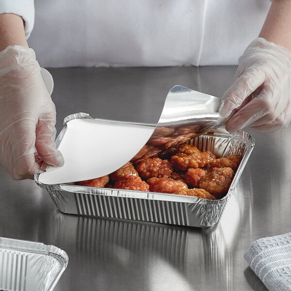 A person in gloves putting food in a Choice oblong foil container.