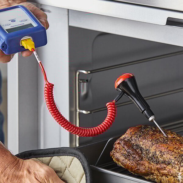 A person using a Comark PK24M/US penetration probe to measure the temperature of meat.