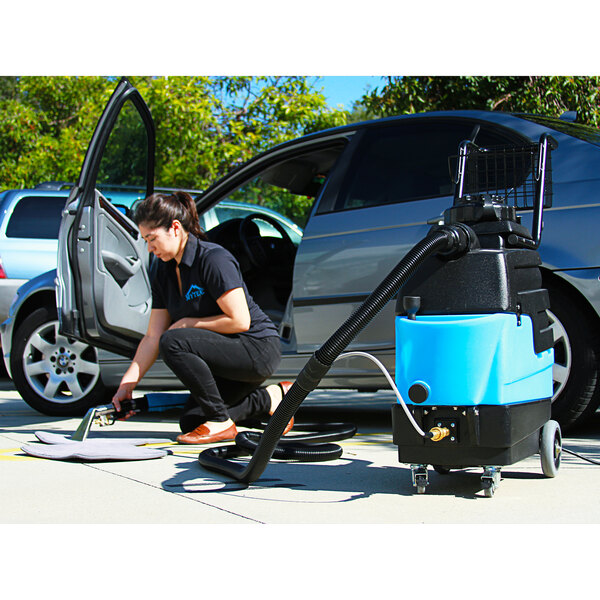 A woman using the Mytee Lite carpet extractor to clean a car's upholstery.