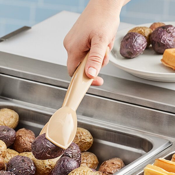 A person using Cambro beige plastic tongs to scoop potatoes into a pan.