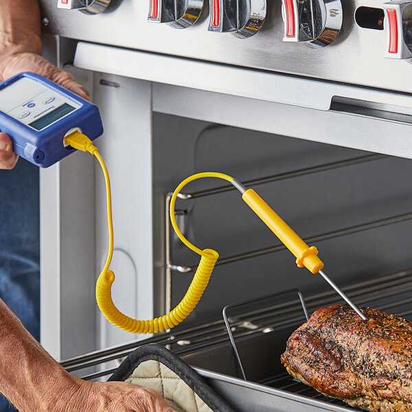 A person using a Comark thermometer with a yellow cable to check the temperature of a meat roast.