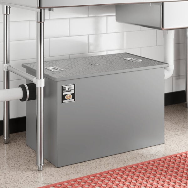 A gray metal Regency grease trap with a metal lid over a sink drain.