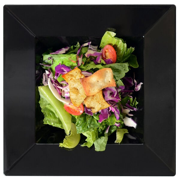 A salad in a Fineline Settings black square bowl with crackers on top.