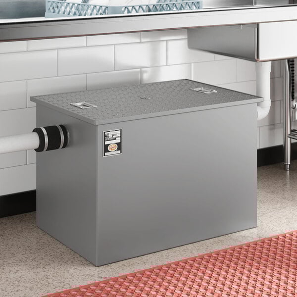 A grey metal Regency Grease Trap with a white pipe coming out of it.