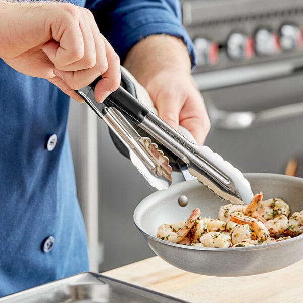 A person using Carlisle stainless steel scalloped tongs to cook shrimp in a pan.