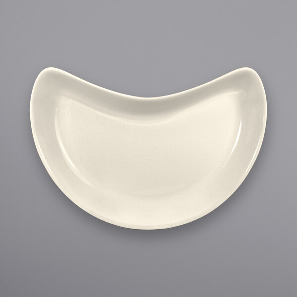 A white International Tableware stoneware crescent dish with a curved edge.