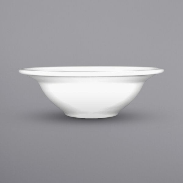 A close up of an International Tableware bright white porcelain grapefruit bowl with a rolled edge.