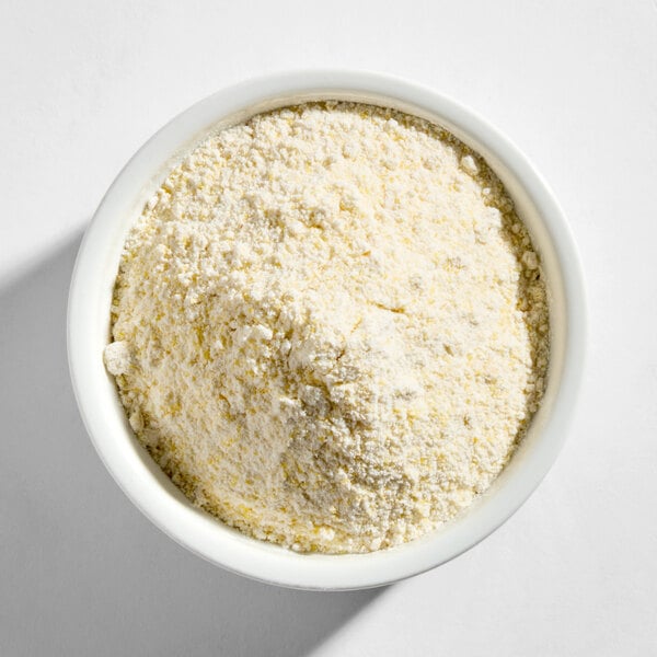 A white bowl filled with a yellowish, granular hush puppy mix with onion.